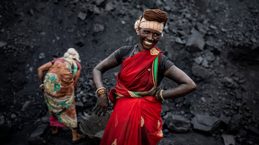 传统中年印度女性当她在煤矿前微笑时，服装双手叉腰